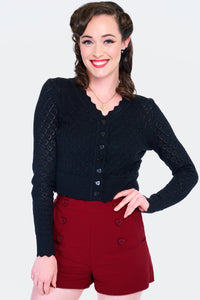 Model wearing black v-neck cardigan with openwork heart design, scalloped edges, and black plastic heart-shaped buttons. Shown from the front buttoned up 