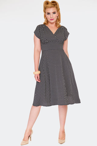 A model wearing a just below the knee length crepe fabric dress with a surplice style v-neckline, fitted waist, and tulip cap sleeves. Pattern of black and white zig-zag stripes with overlapping lines similar to basketweave. Shown from the front