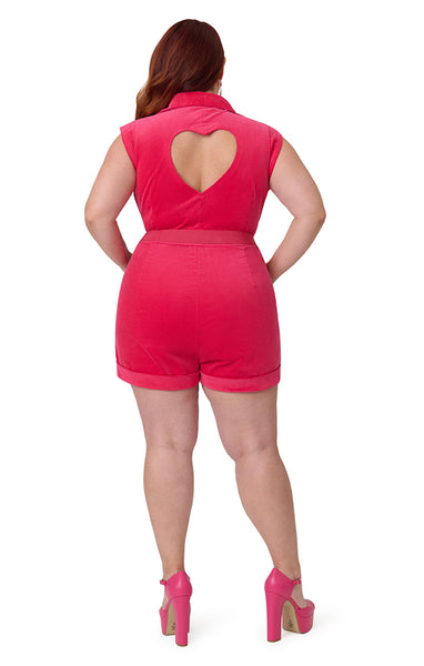 Plus size model wearing a hot pink lightweight corduroy romper with pointed collar, cap sleeves, slight v-neckline, front zip closure, heart cutout at back, matching canvas belt with gold heart buckle, side seam pockets, and shorts. Shown from back