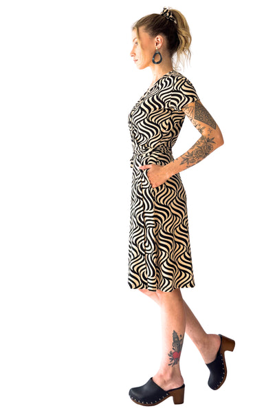 ivory and black swirly optical print cap sleeve knee length wrap dress, shown side view on a model