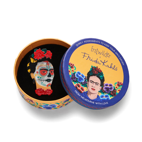 Frida Kahlo Collection “Frida Calavera” layered resin portrait brooch, showing Frida with red flowers in her hair and at her throat, and calavera face paint, shown in illustrated round box packaging
