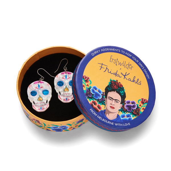 pair of Frida Kahlo Collection “Dia De Los Muertos” layered resin calavera skull dangle earrings, shown in illustrated round box packaging