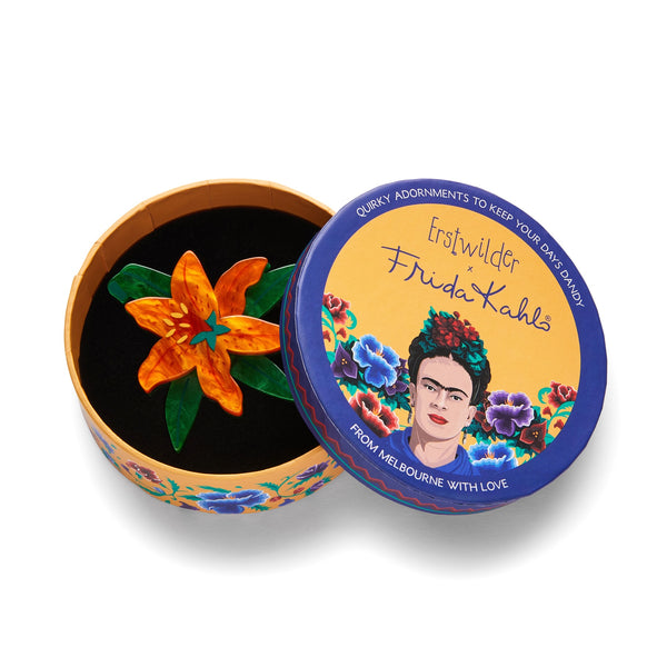 Frida Kahlo Collection “Strange As You” orange tiger lily blossom and green leaves layered resin brooch, shown in illustrated round box packaging