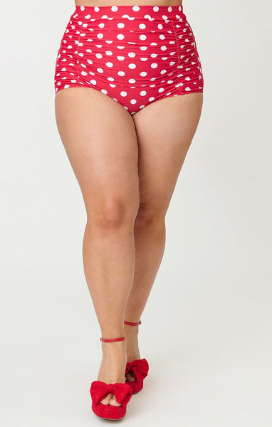 Bright red and polka dot patterned 50s style high-waist ruched front swim bottoms, shown on plus size model from front in close up