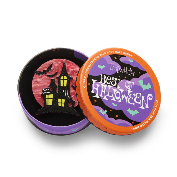 spooky black mansion silhouetted against a ruby full moon "On Haunted Hill" layered acrylic resin brooch, shown in illustrated round box packaging