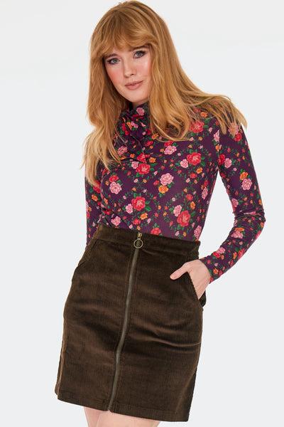 a model wearing a brown corduroy high-waisted mini skirt with side seam pockets and front zip closure with brass tone o-ring zipper pull. Shown from the front