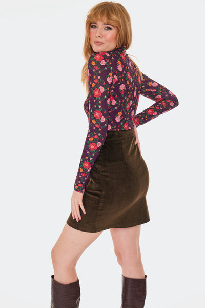 a model wearing a brown corduroy high-waisted mini skirt with side seam pockets and front zip closure with brass tone o-ring zipper pull. Shown from the back