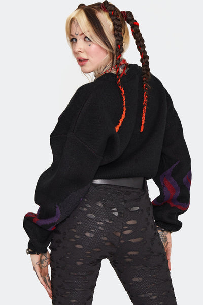 a model wearing a thick jacquard knit sweater with an oversized cropped fit. It has a purple and red flame pattern on a black background across the chest and sleeves. Shown from back