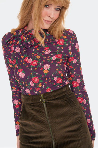 a model wearing a brown corduroy high-waisted mini skirt with side seam pockets and front zip closure with brass tone o-ring zipper pull. Shown from the front in close up