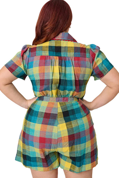 Plus size model wearing cotton red, blue, and yellow Madras plaid print romper with pointed collar with red rickrack trim and red plastic button-up bodice, puffed short sleeves, and pleated relaxed fit shorts with side seam pockets and matching buttons down side of left hip. Shown from back in close up