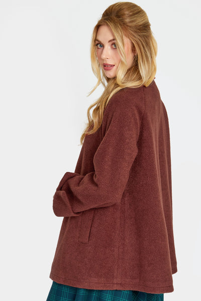 a model wearing a warm brown swing coat made of a thick textured faux wool. It has a pointed fold over collar, slash pockets, three self buttons, and sleeves with notched cuffs. Shown closed from back