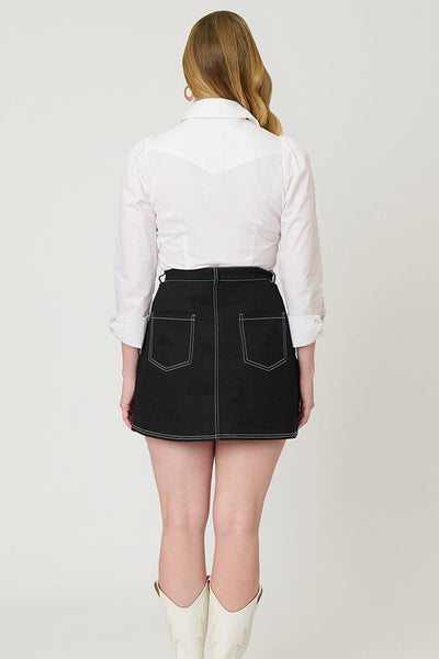 Model wearing a black denim a-line mini skirt with contrasting warm white stitching running vertically down skirt with white star embroidery on each hip and zipper/button front closure. Shown from back to display back pockets of skirt
