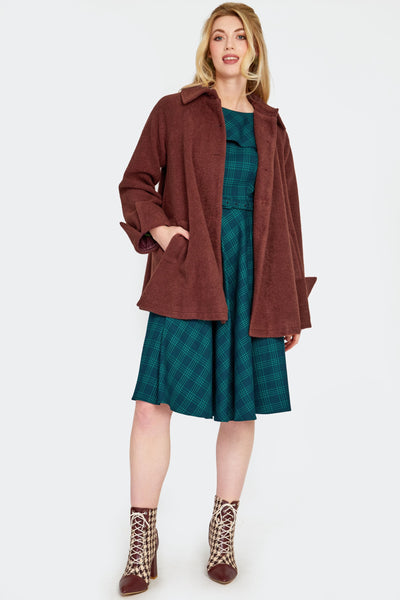 a model wearing a warm brown swing coat made of a thick textured faux wool. It has a pointed fold over collar, slash pockets, three self buttons, and sleeves with notched cuffs. Shown open from front