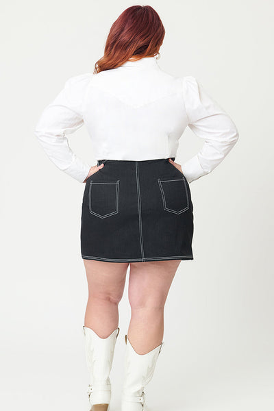 Model wearing a black denim a-line mini skirt with contrasting warm white stitching running vertically down skirt with white star embroidery on each hip and zipper/button front closure. Shown from back to display back pockets of skirt