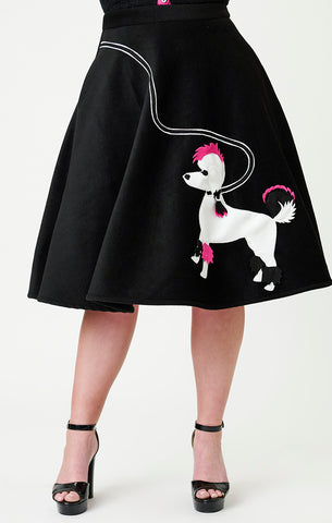 model wearing black felt style fabric swing skirt with pink, white, and black felt applique of Gonk, Elvira's poodle at bottom left hem with black and white leash applique running to right hip of skirt. Shown from front from waist down