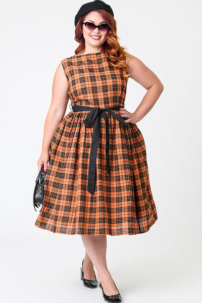 Plus size model wearing a cotton orange, black, and yellow gold lurex plaid patterned swing dress with slash neckline, darted bodice, black cotton sash belt, and below the knee gathered skirt. Shown from front