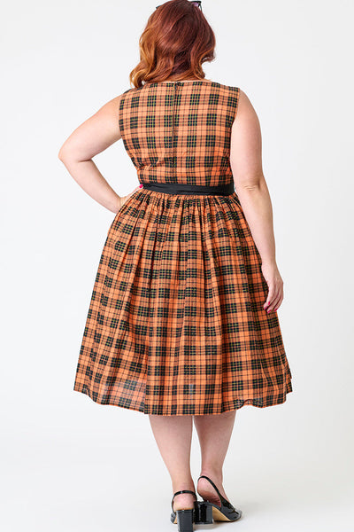 Plus size model wearing a cotton orange, black, and yellow gold lurex plaid patterned swing dress with slash neckline, darted bodice, black cotton sash belt, and below the knee gathered skirt. Shown from back