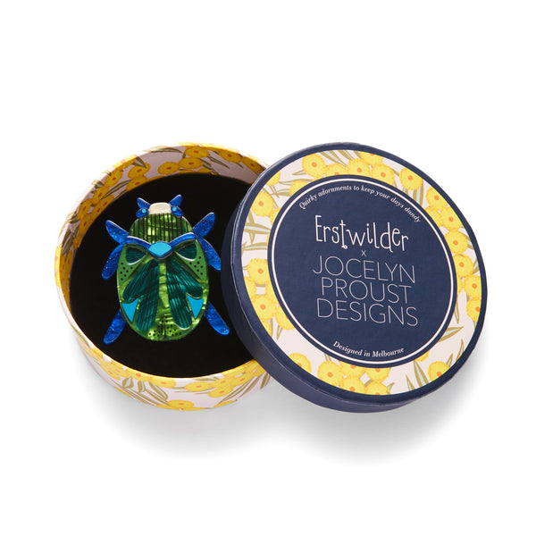 Jocelyn Proust Collaboration Collection "Luck of the Beetle" layered resin blue and green brooch, shown in illustrated round box packaging