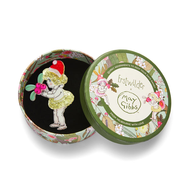 May Gibbs Christmas Collection "Native Berries Christmas" layered resin brooch depicting a standing gumnut baby in santa hat holding holly sprig, shown in illustrated round box packaing
