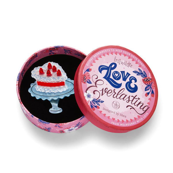 Love Everlasting Shea O'Connor collaboration collection "Piece of Cake" heart-shaped caked on a blue pedestal layered resin brooch, shown in illlustrated round box packaging