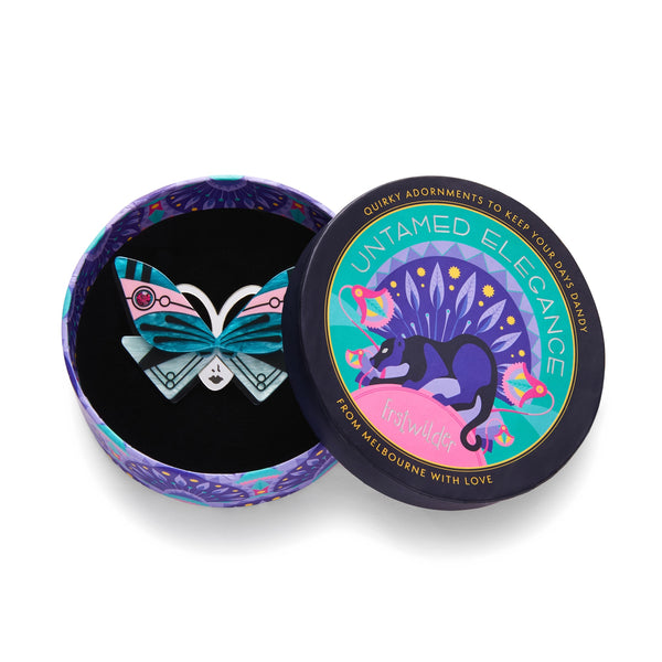 Untamed Elegance Collection "Butterfly Sonata" blue, pink, black, white, and mirror finish silver layered resin brooch depicting an Art Deco style butterfly as a mask on a lady's face, shown in illustrated round box packaging