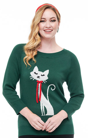 Model wearing a forest green jacquard knit sweater with scoop neckline, three quarter sleeves, and ribbed detail at cuffs and neck. It has a knit image of a white 60s style cat with a red bow around its neck- the bow is a knit appliqué. Shown from front untucked