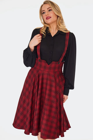 a model wearing a red plaid swing skirt with attached matching suspenders. The suspenders are attached at the front with two black plastic buttons. Shown from front