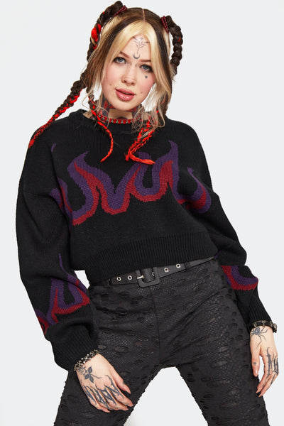 a model wearing a thick jacquard knit sweater with an oversized cropped fit. It has a purple and red flame pattern on a black background across the chest and sleeves. Shown from front 