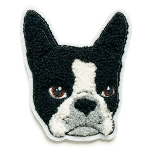 A fuzzy chenille patch of the head of a black and white Boston Terrier dog. It’s head is chenille fabric and its eyes are brown embroidered thread. The patch has a white felt border.