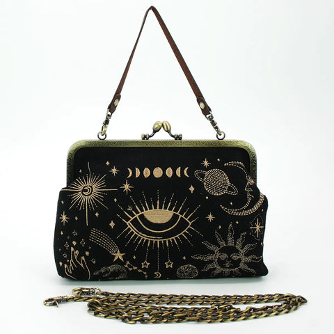 A vintage inspired handbag with an antiqued bronze metal kiss lock enclosure. The body of the purse is black fabric with gold embroidered planets, stars, moon phases, and hands. The handle is a detachable faux leather strap and in front of the bag is the antiqued bronze metal shoulder strap.