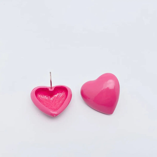 shiny pink enameled metal heart-shaped post earrings. One earring is shown backwards to display the post ear attachment