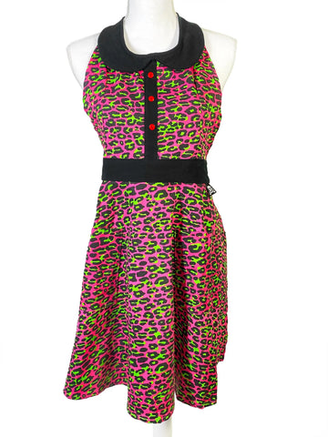 Retro-style full coverage bib front apron in flashy neon pink and green leopard print with two handy front patch pockets, finished with black waistband tieback closure, peter pan collar and button placket detail