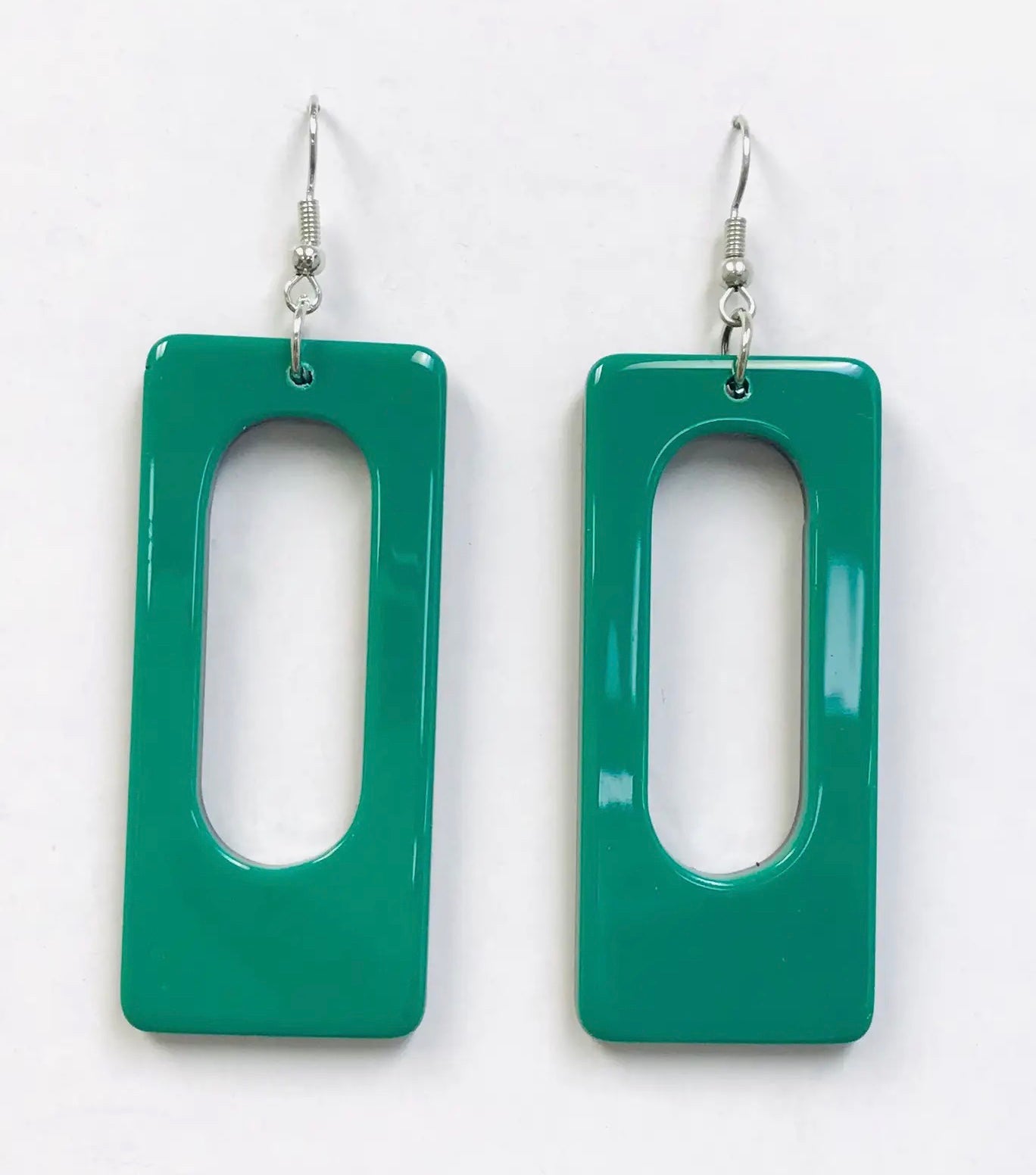 A pair of rectangular acrylic dangle earrings with rounded corners and an oblong hole in the middle. The front of the earring is a rich green color with black on the back 