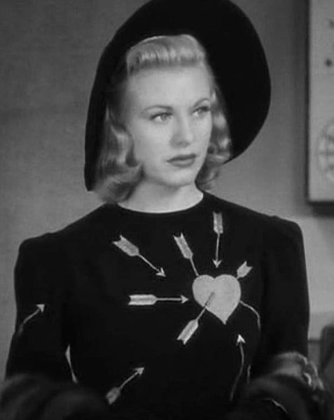 black and white photo of Ginger Rogers as her character Amanda Cooper in the 1938 film Carefree, wearing a black dress with embroidered heart and arrows design on the bodice