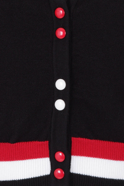 short sleeve v-neck cardigan in black, red, and white with alternating sets of red and white buttons, striped band detail at waist and sleeves, and geometric design collar, showing close up swatch of buttons and bottom band