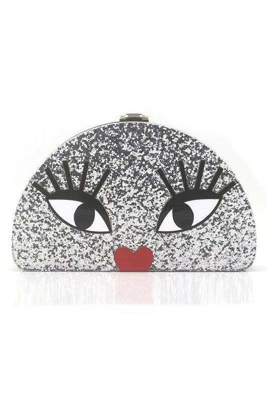 A clutch purse in a rounded crescent shaped with large cartoon eyes and a red top lip. The background of the purse is large flakes of silver glitter encased in clear resin. This is a front facing view of the purse. 