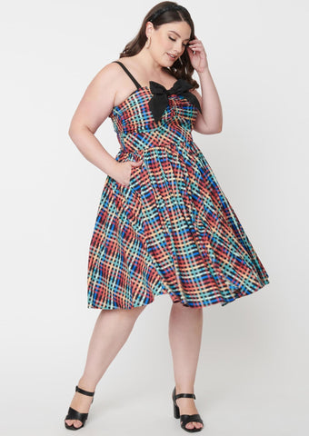 rainbow madras plaid 50s style fit & flare silhouette sundress featuring a princess-seamed bodice with ruched bust sweetheart neckline, applied big black bow and elasticized smocked back panels, removable adjustable straps, and a full swing skirt with side seam pockets in a below the knee length, shown on model