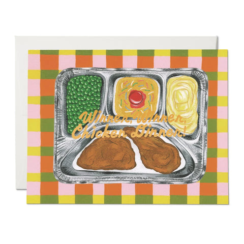 Greeting card of a silver TV dinner tray with chicken, peas, mashed potatoes, and cake. “Winner, Winner, Chicken Dinner” written in gold script on the middle of the card with a yellow, pink, green, and orange checkered background