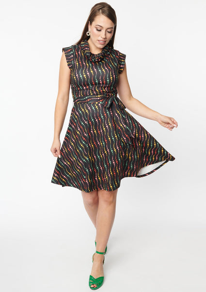 A fit and flare dress with a cowl neck and cap sleeves. It has a pattern of swirled dots in red, green, yellow, and blue on a black background. Shown on a model posed with the skirt flared out