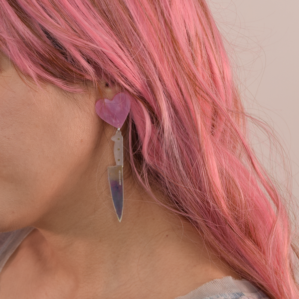 clear holographic acrylic chef's knife suspended from pearly pink heart drop earring, shown on model