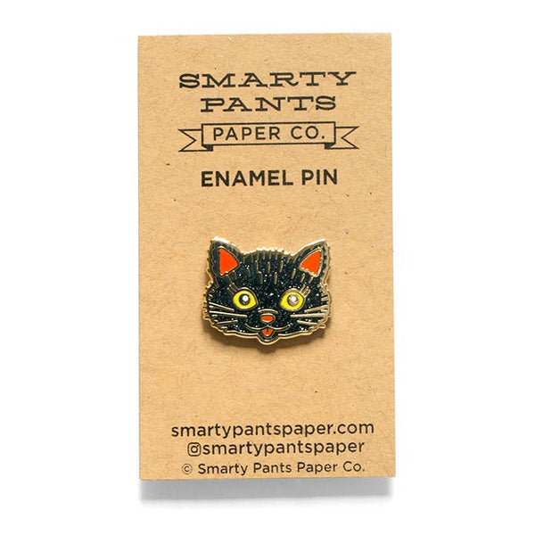 glitter black cat face with yellow eyes and orange details enameled gold metal lapel pin, shown on illustrated cardstock backer packaging