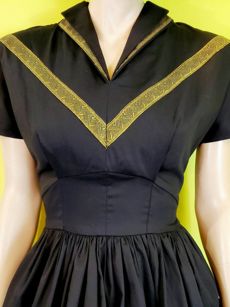 50s style Patio Dress in black stretch cotton sateen embellished with metallic gold ribbon trim features a collared v-neckline, fitted princess seamed bodice, short dolman sleeves, and gathered full  just-below-the-knee length skirt. shown close up of bodice on mannequin