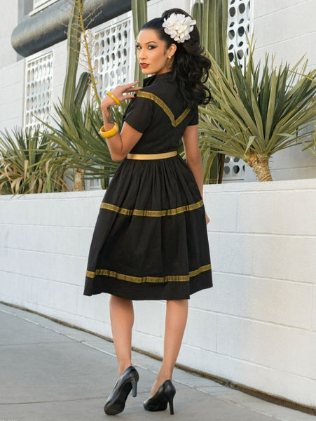 50s style Patio Dress in black stretch cotton sateen embellished with metallic gold ribbon trim features a collared v-neckline, fitted princess seamed bodice, short dolman sleeves, and gathered full  just-below-the-knee length skirt. shown on model