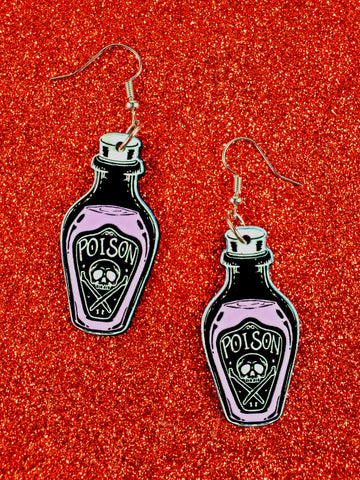A pair of acrylic coated dangle earrings in the shape of bottles with a “Poison” label on them