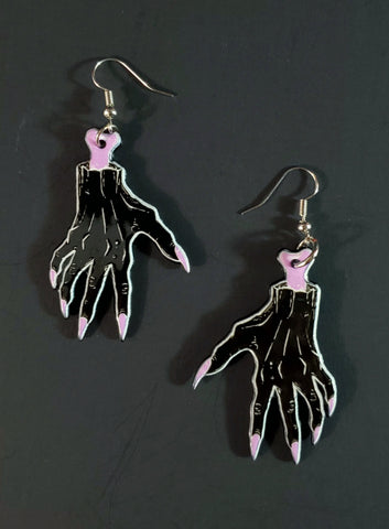 A pair of printed dangle earrings coated in acrylic resin- each earring has a severed hand with exposed pink bone and long pink fingernails 