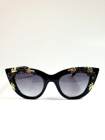 Thick black plastic cat-eye sunglasses with striking ornate gold metal leaf and black floral details on both the frame front and arms