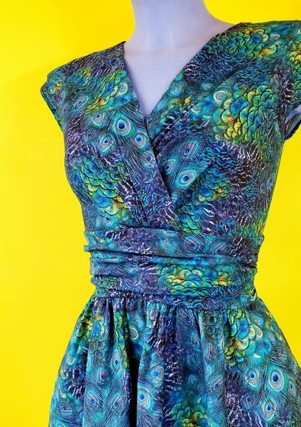 cap sleeve cotton dress in a green and blue peacock feather print with a surplus gathered neckline, wide gathered waist, and a just past the knee full skirt, showing torso close-up on a mannequin