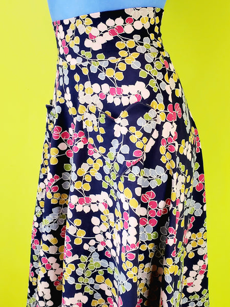 stretch cotton knit high-waisted midi length skirt is in a navy blue background multi-color stylized floral print and features a wide waistband and heart-shaped patch pockets. shown waist down 3/4 view close up of pockets on a mannequin.