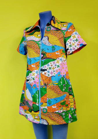 short sleeve zip-front cotton a-line mini dress with wide pointed collar and patch pockets in a multicolored landscape print of psychedelic patterns, including pinwheels, apples, hands, trees, frogs, cows, and more. shown on a mannequin.