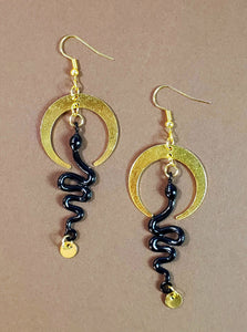 gold metal dangle earrings in the shape of a stylized downward facing crescent moon with an enameled black snake charm dangling from the middle